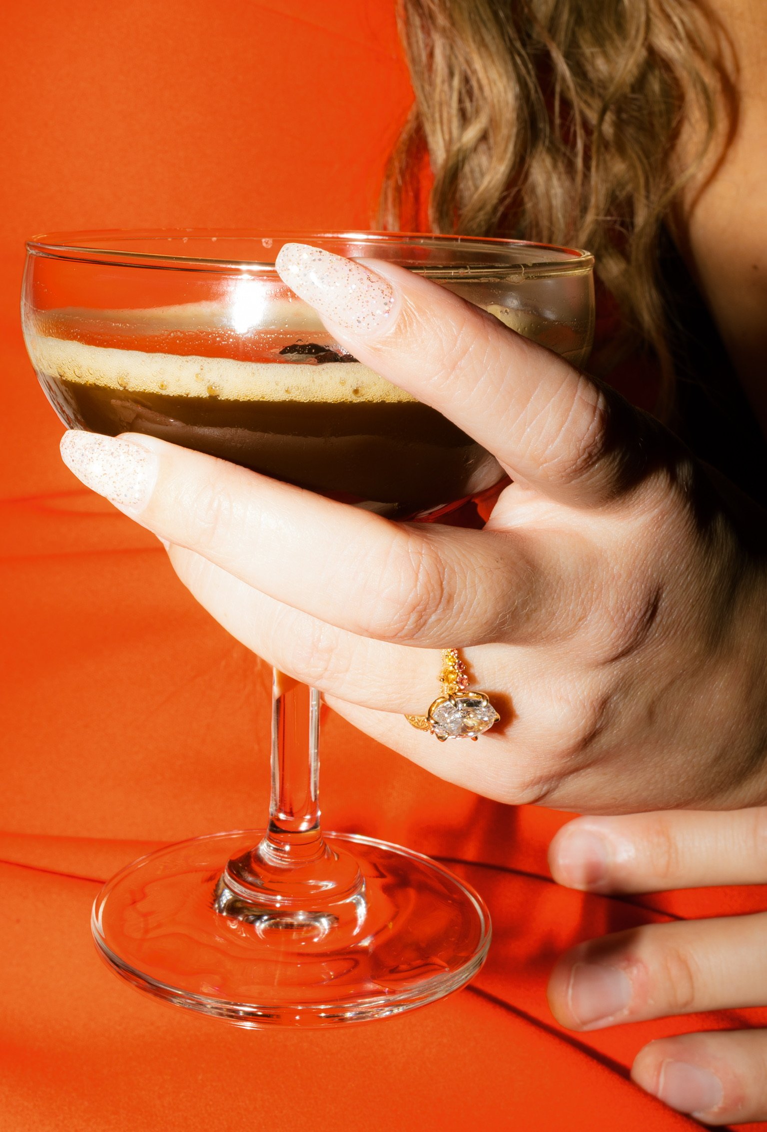 Close up: Nicole’s ringed hand holding an espresso martini against her red dress.