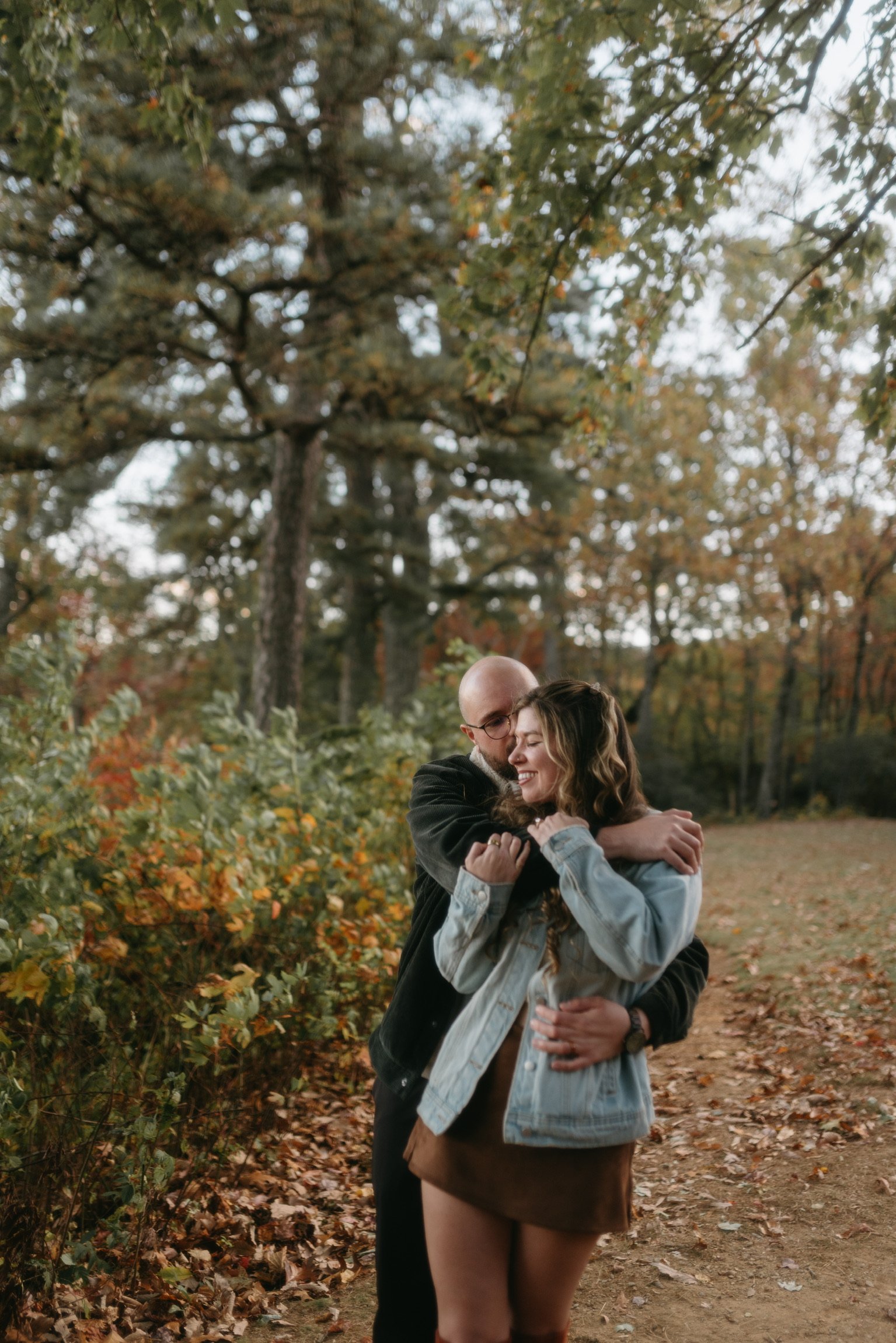 Ian holding Nicole close on the woodland path, both laughing.