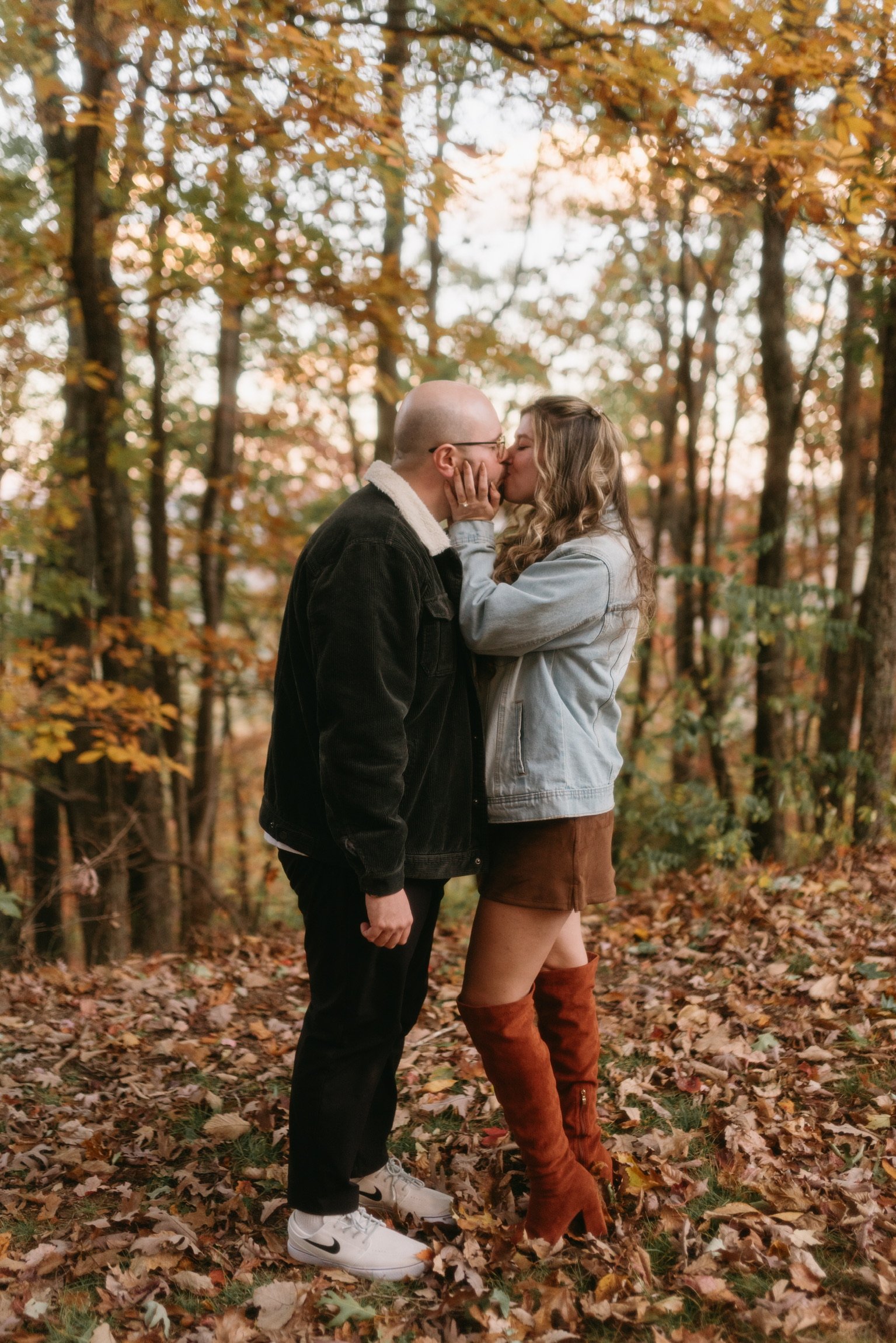 Nicole and Ian kissing among the autumn trees, her rust boots deep in the leaves.