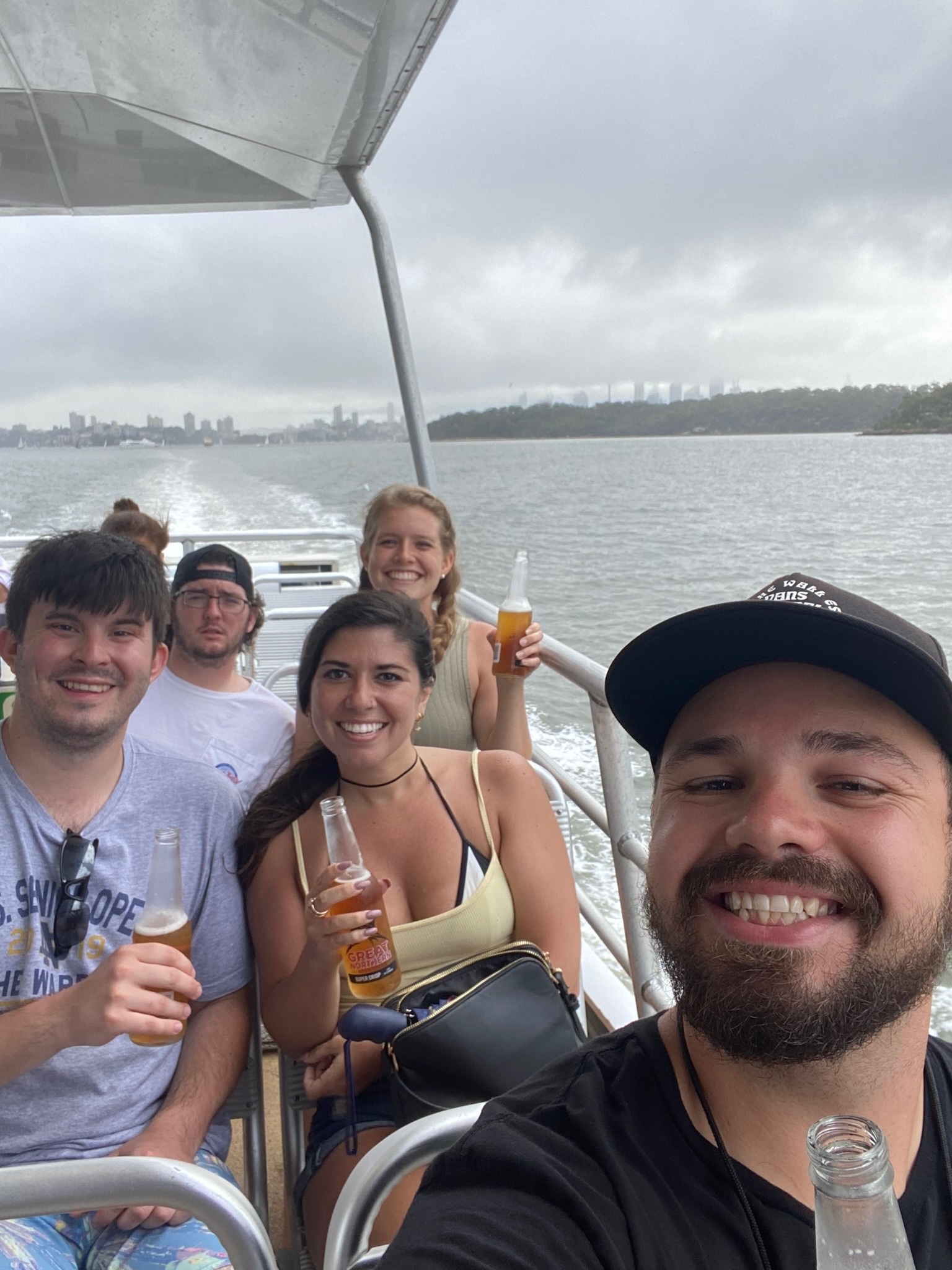 A selfie of friends with beers on the back deck of a harbor ferry under gray skies.
