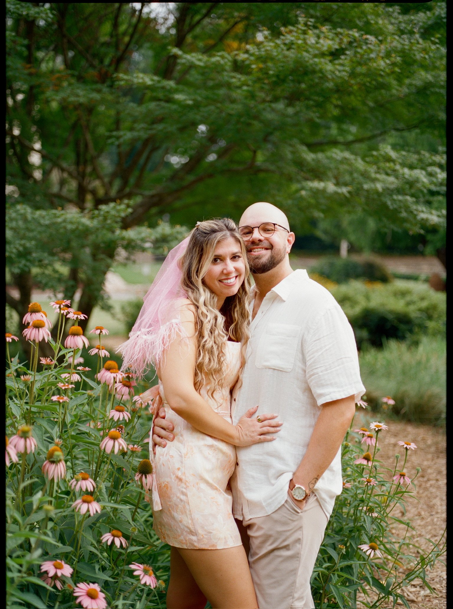 Nicole in her pink veil and Ian smiling at the camera among pink coneflowers.
