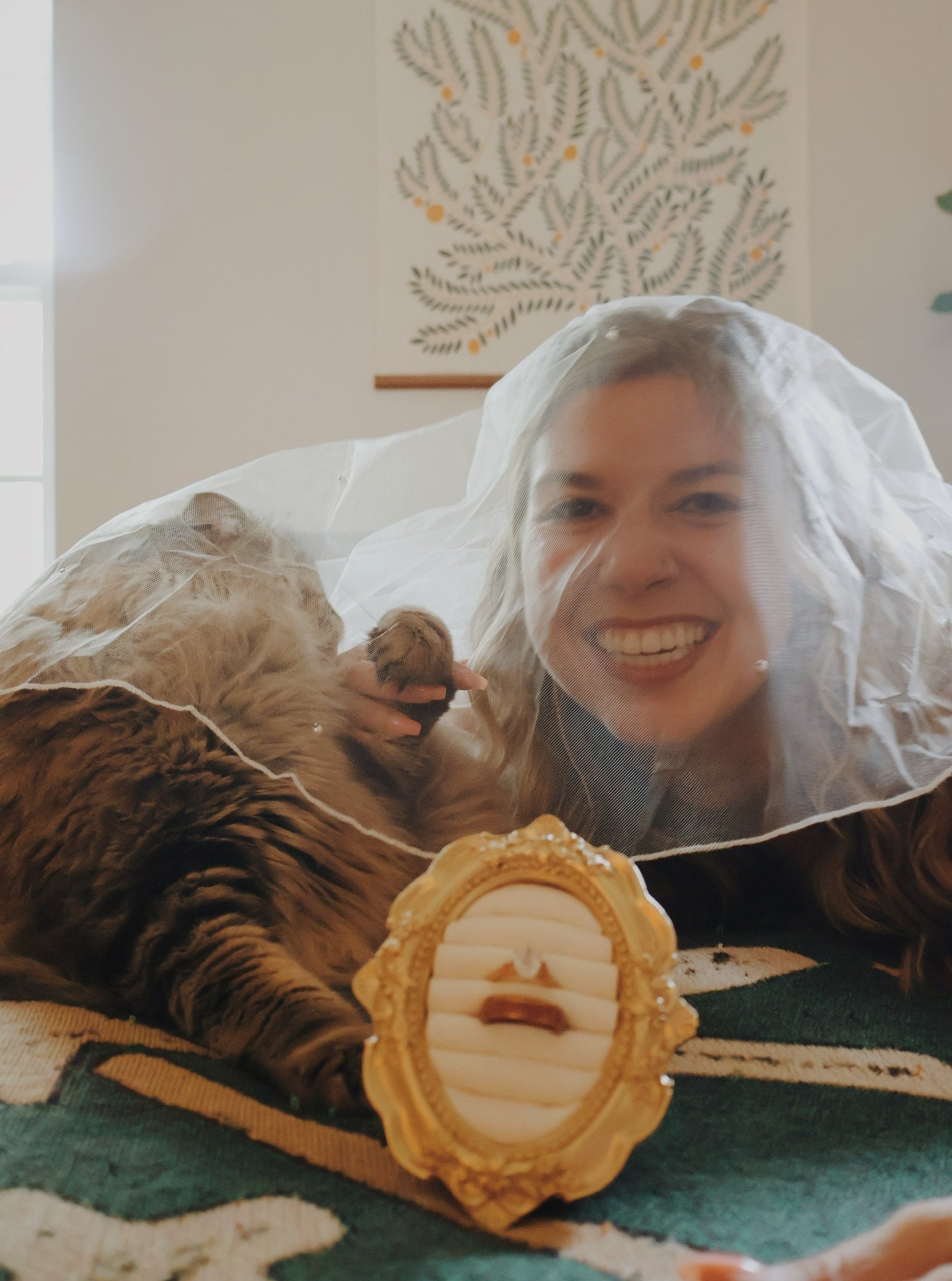 Nicole grinning at the camera from under the veil, the tabby cat beside her.