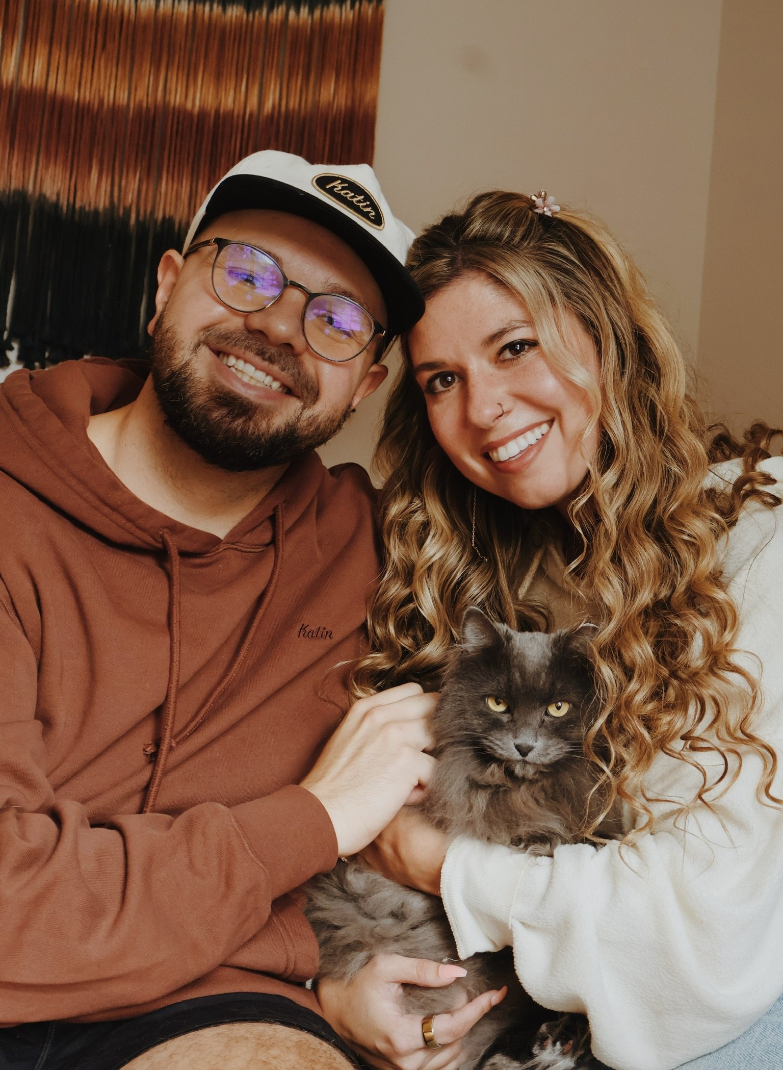 Nicole and Ian cheek to cheek, the gray cat held between them.