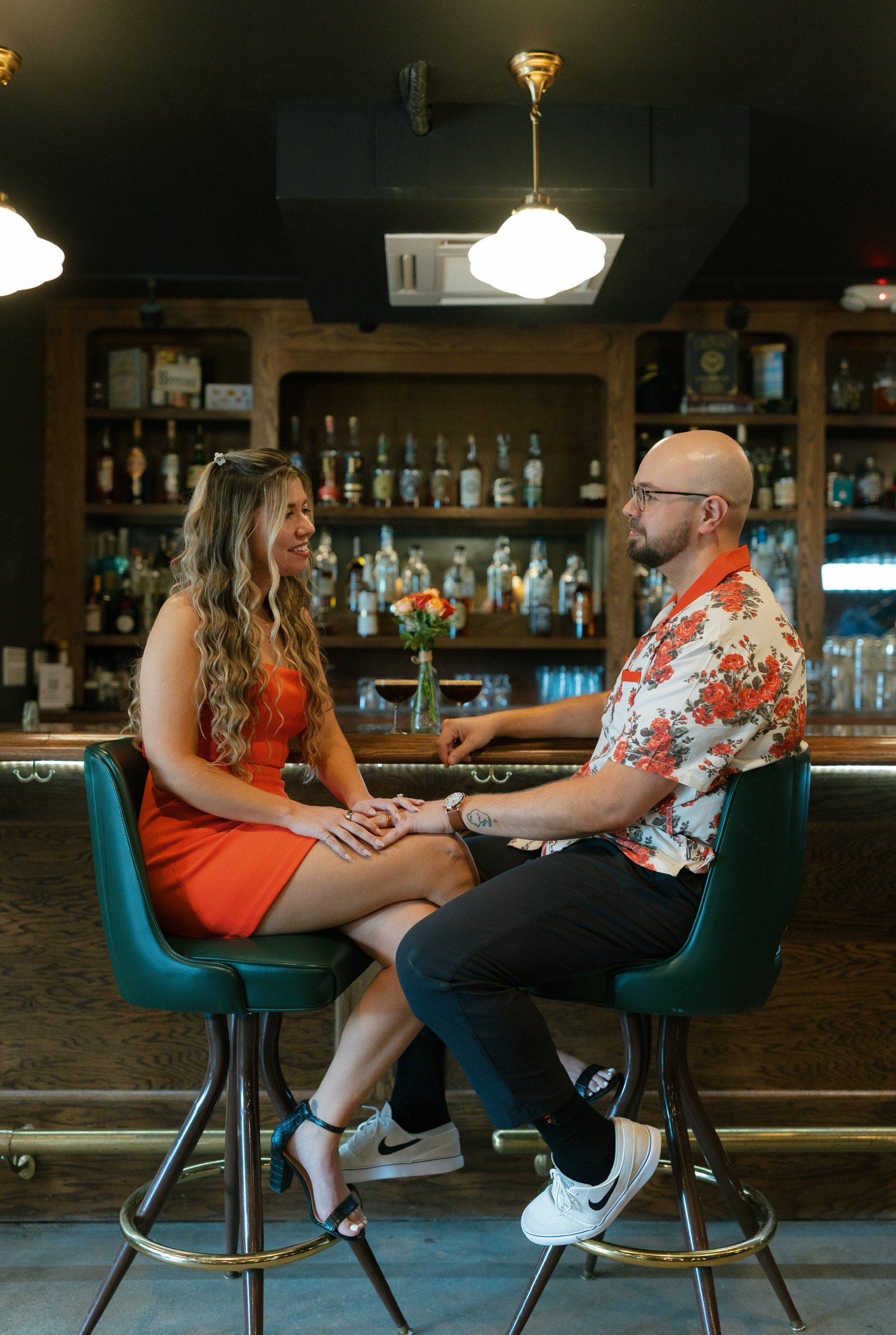Nicole and Ian on green bar stools at Wolfe & Porter, knees touching, the back bar’s bottles glowing behind them.