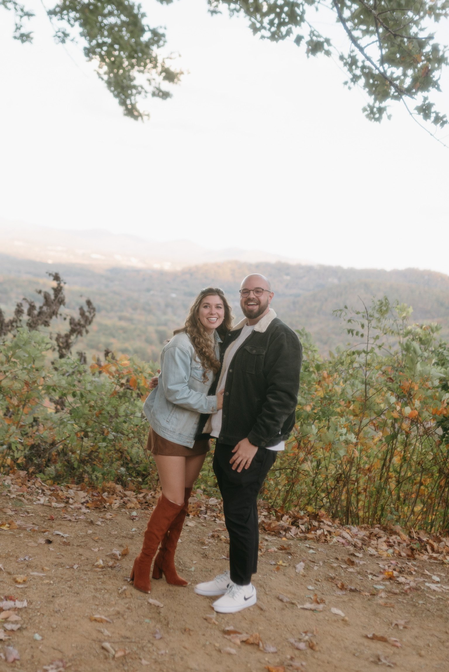 Nicole and Ian standing side by side, both grinning, autumn scrub around them.