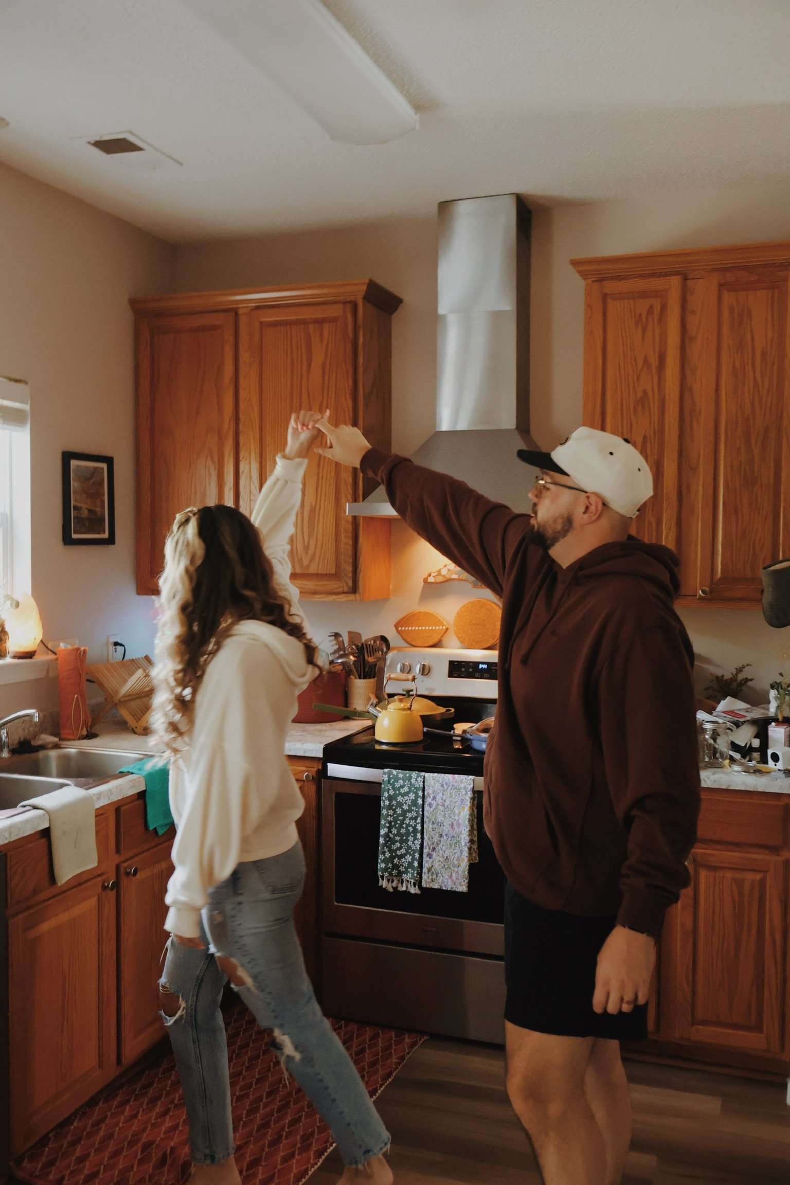 Ian twirling Nicole in their wood-cabinet kitchen.