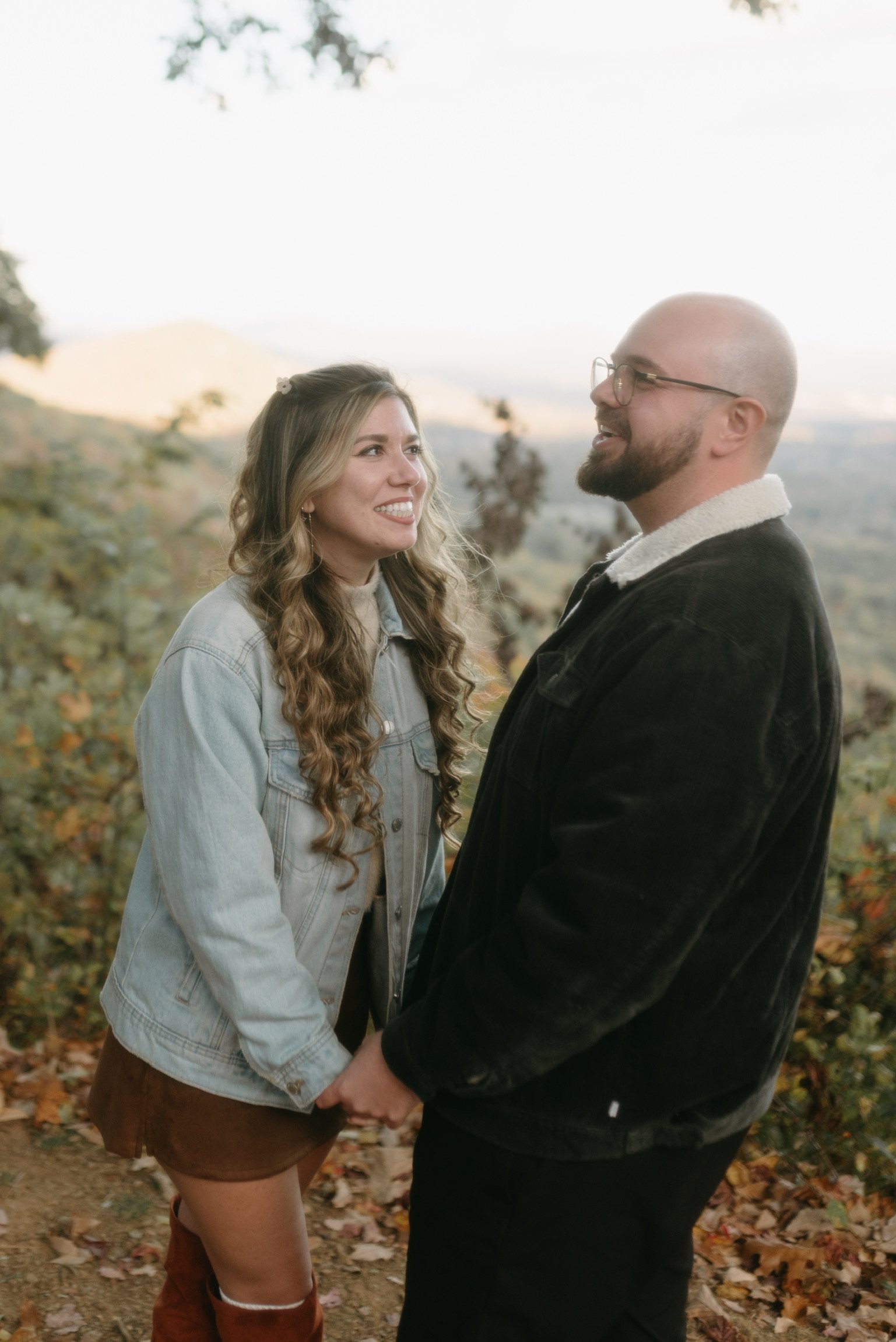 Nicole and Ian hand in hand, smiling at each other, the ridgeline behind.