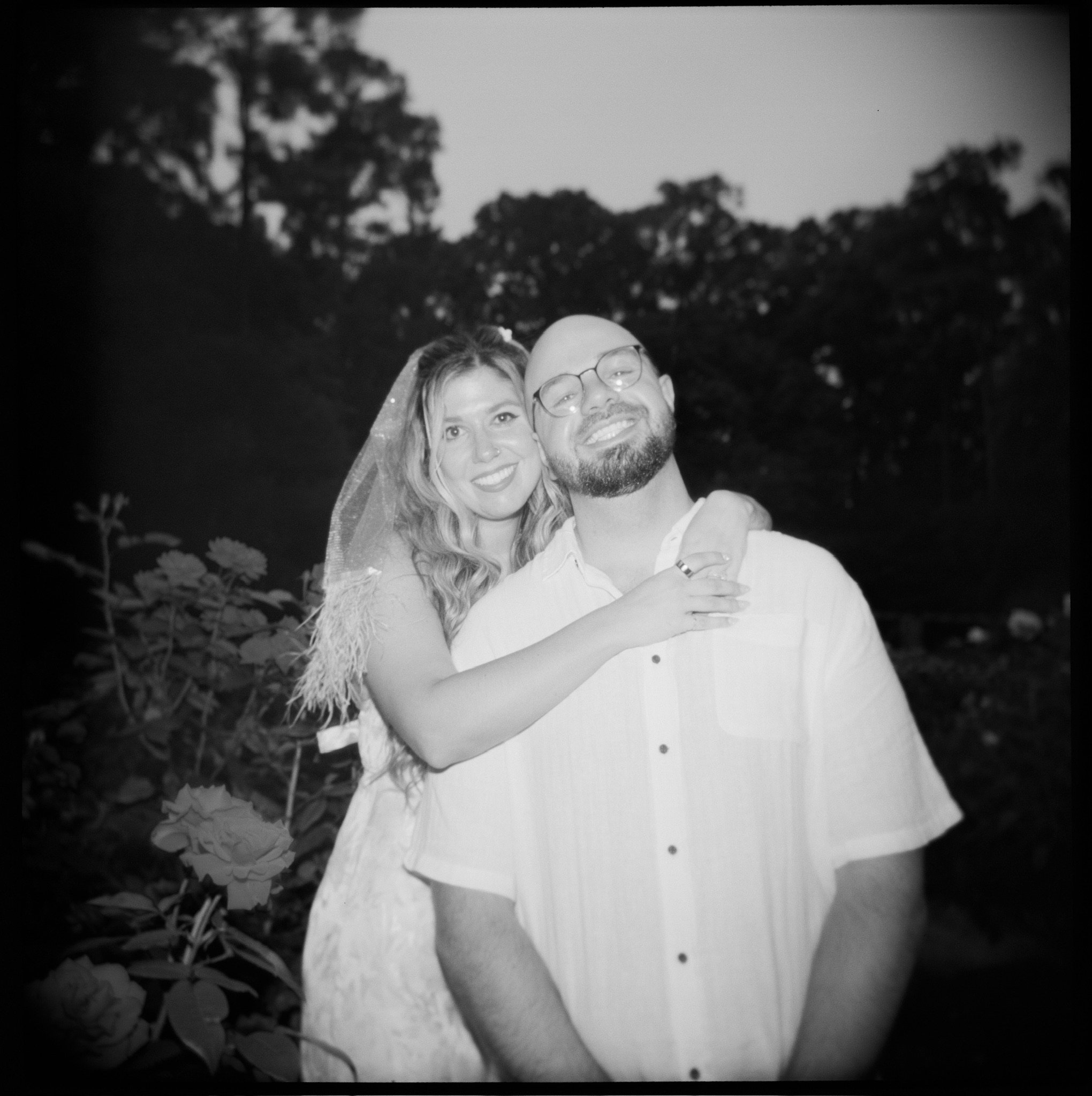 In black and white, at dusk: Nicole hugging Ian from behind, both smiling.