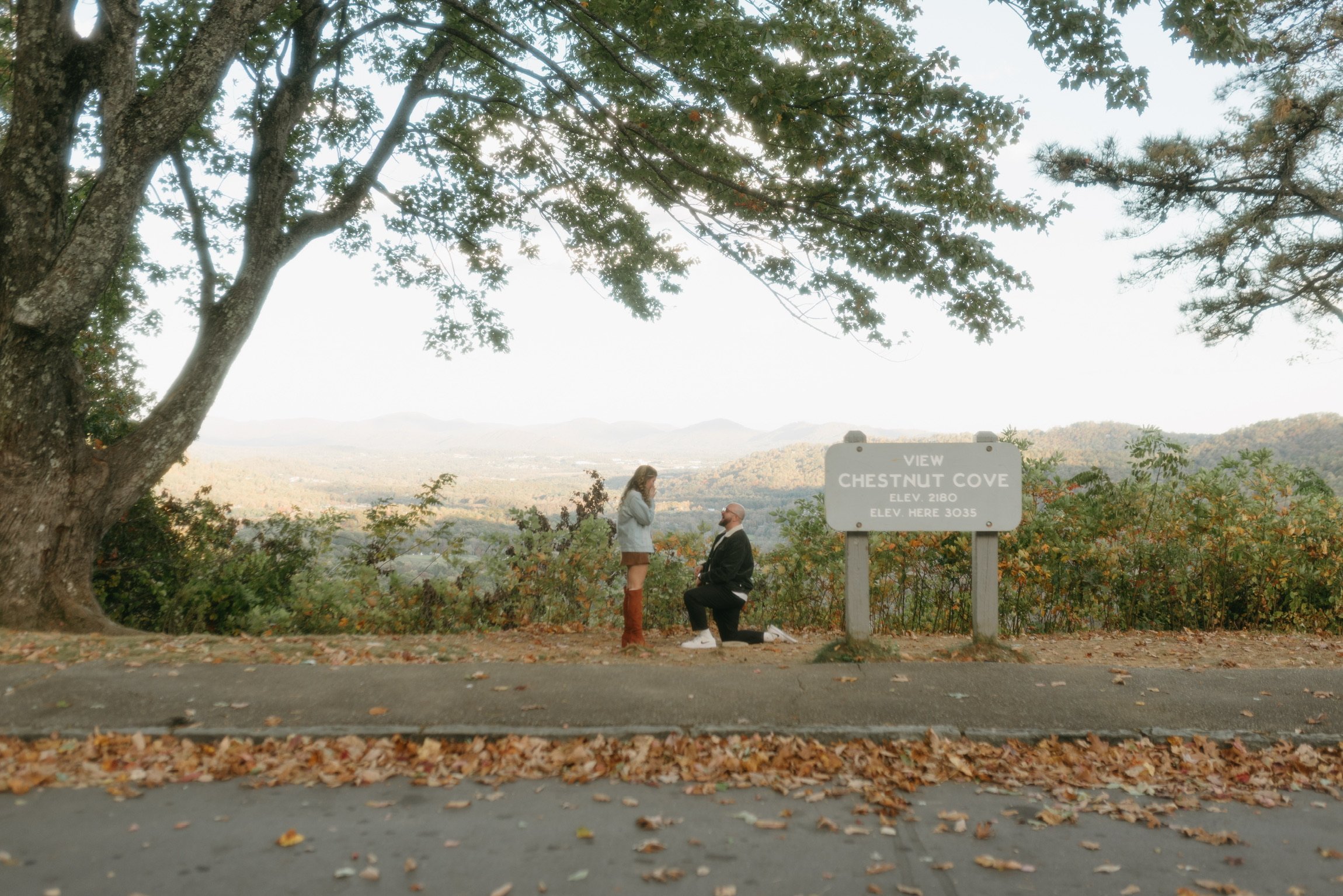 The same overlook from across the road: Ian down on one knee beside the Chestnut Cove sign.