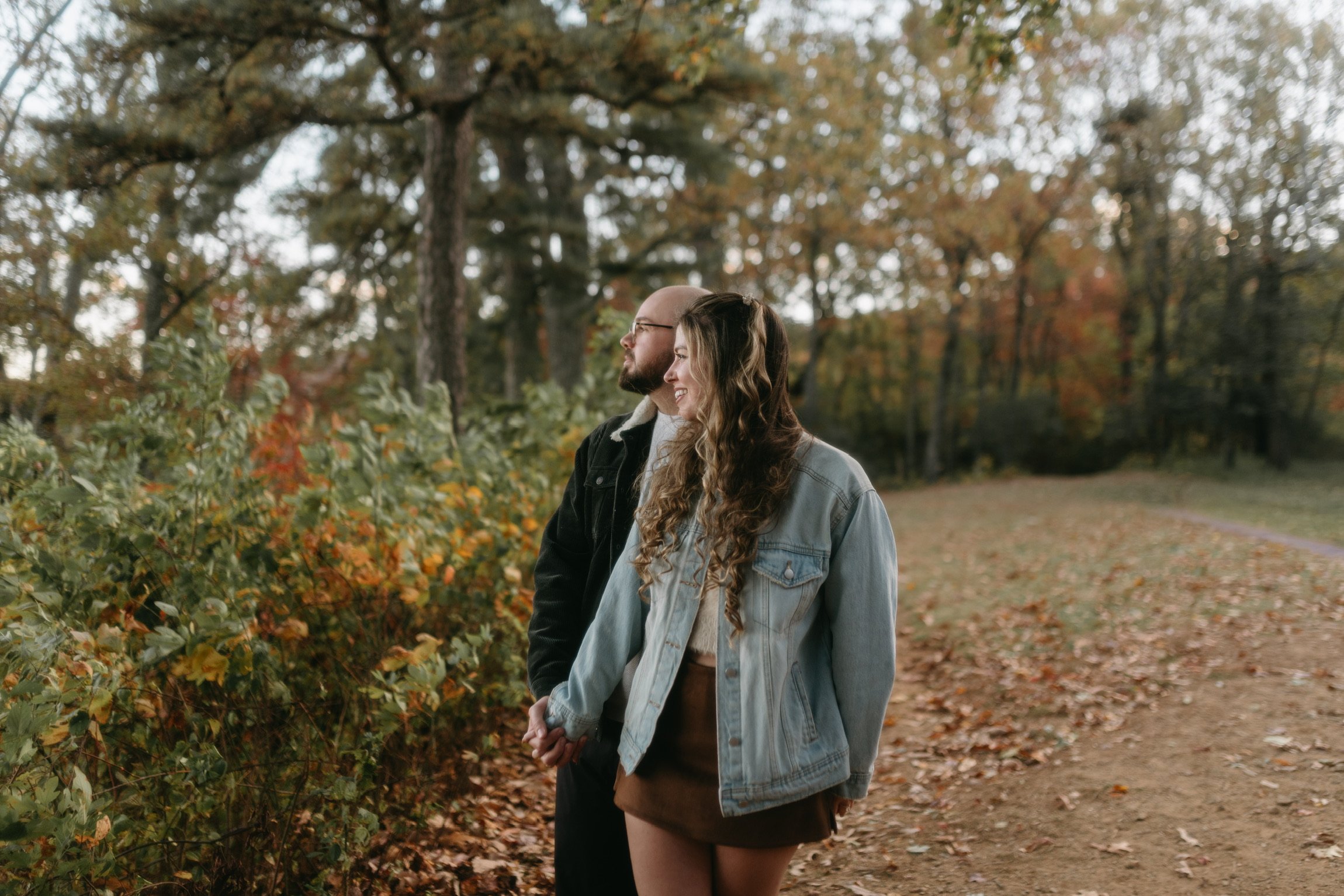 Nicole and Ian walking a leaf-covered path through autumn woods.
