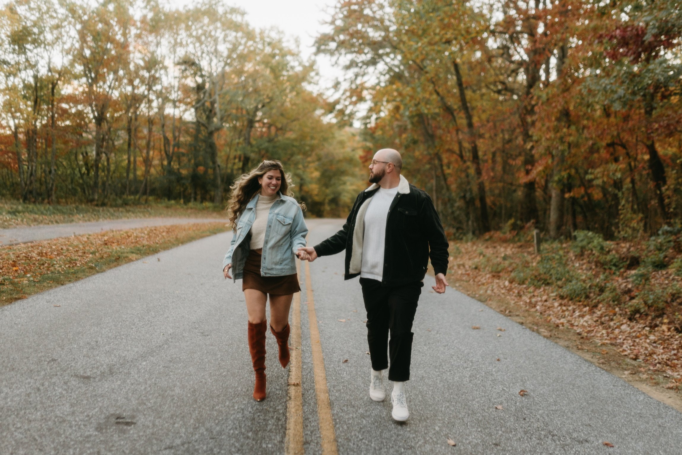 Nicole and Ian walking hand in hand down the middle of the empty parkway, the trees turning on both sides.
