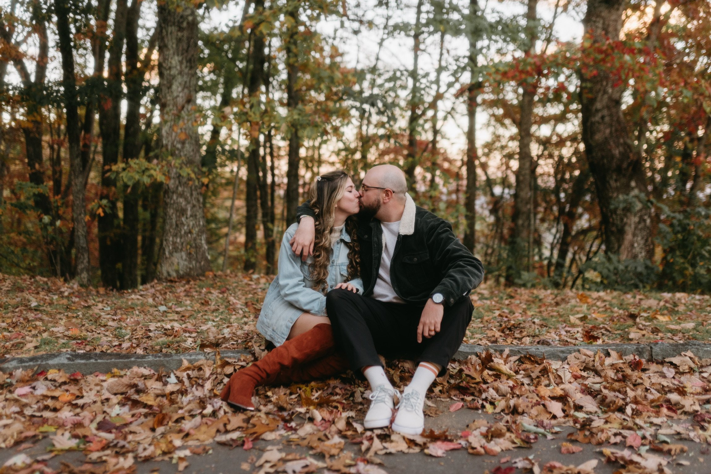 Nicole kissing Ian’s cheek as they sit together in the fallen leaves.