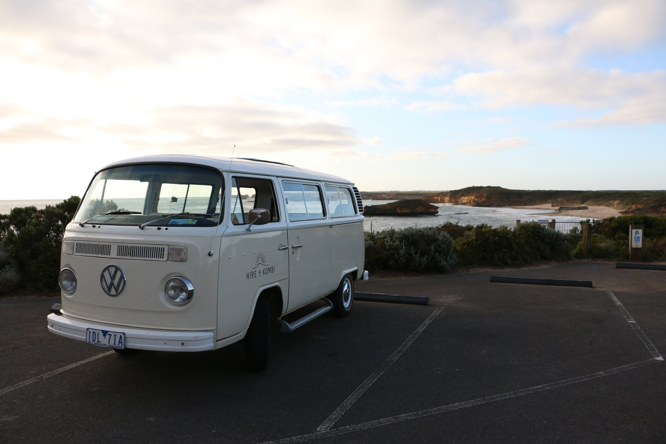 Harriet, the cream VW kombi, parked at a coastal lookout with the sea and a headland behind her.