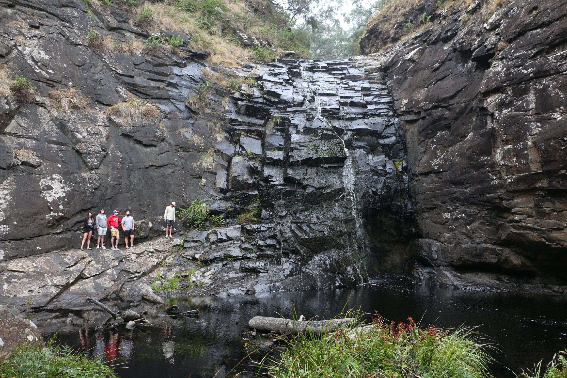 Small figures at the foot of a waterfall spilling down a dark rock gully.